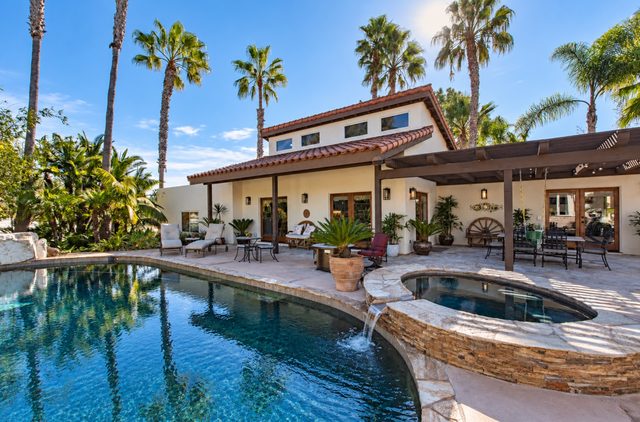 Pool, spa and shaded terrace of a Spanish-style home under palm trees